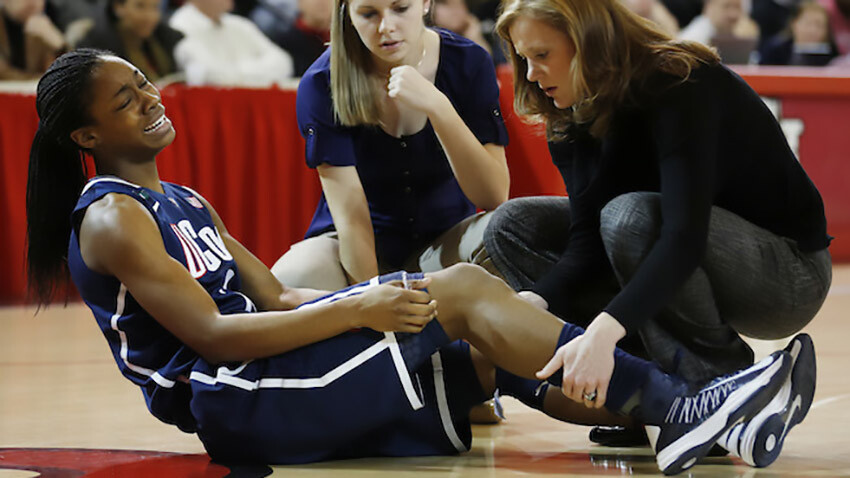 NCAA Player with knee injury on hardwood gym flooring